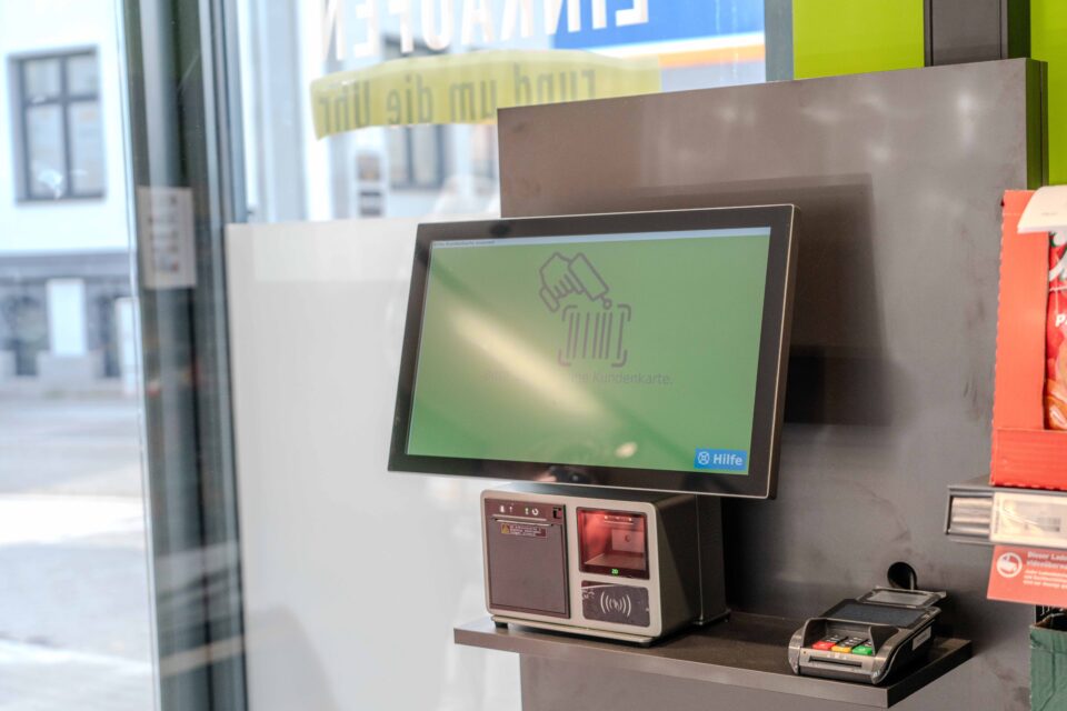 Ein Touchscreen-Selbstbedienungs-Kiosk mit Kartenleser und Scanner in der Nähe eines Schaufensters in einem Geschäft.