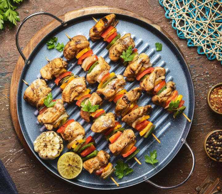 Gegrillter Hähnchen Kebap-Spieß und Gemüsespieße auf einer runden Grillpfanne, garniert mit Petersilie, Zitrone und Knoblauch.