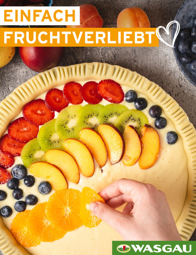 Eine Hand dekoriert ein sommerliches Sommer Dessert, indem sie eine Fruchttarte mit frischen Früchten verziert. Text: 