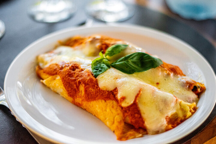 Eine mit Käse überbackene Cannelloni-Enchilada mit Tomatensauce und frischem Basilikum auf einem weißen Teller.
