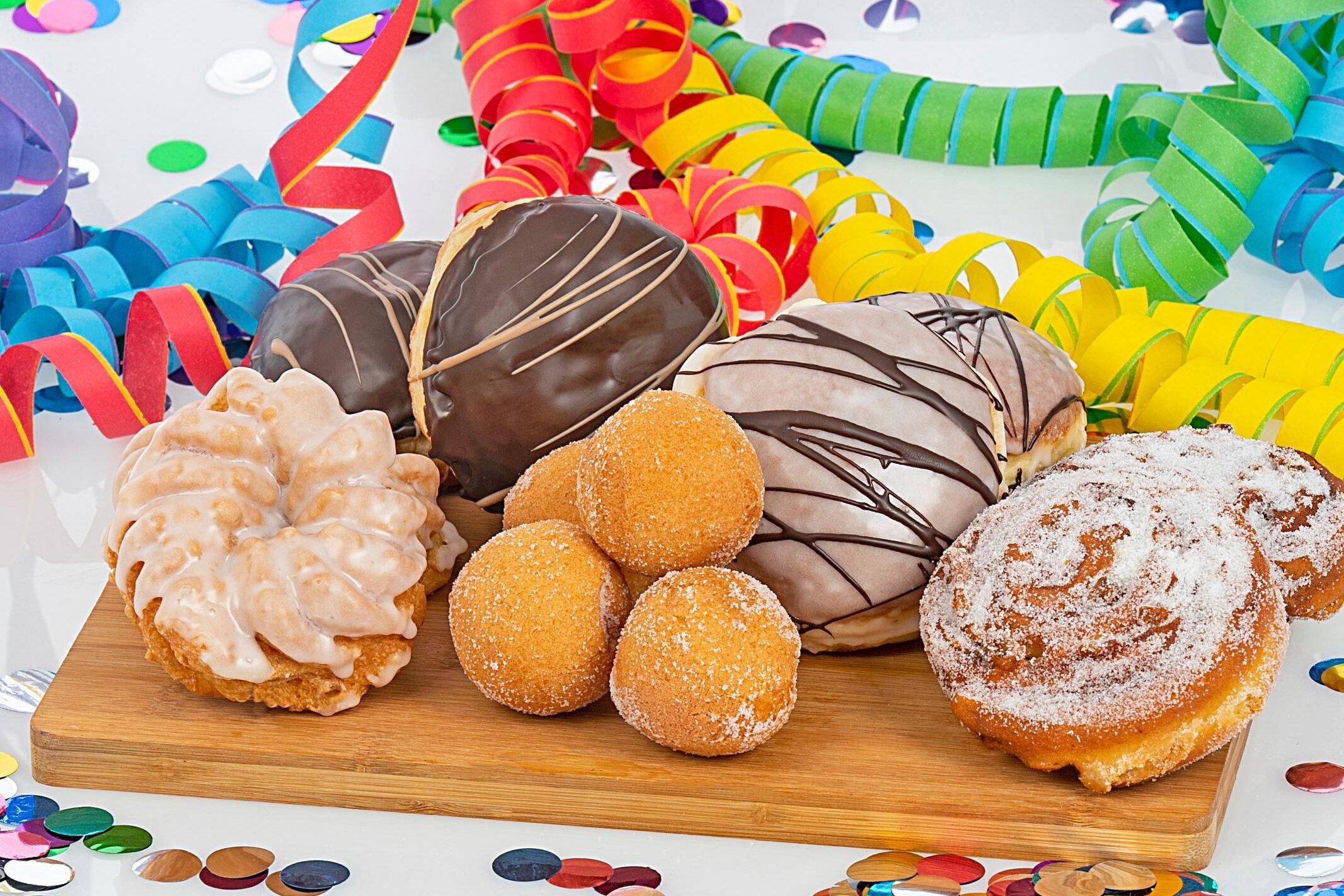 Gemischtes Gebäck und Donuts auf einem Holzbrett mit bunten Luftschlangen und Konfetti im Hintergrund.