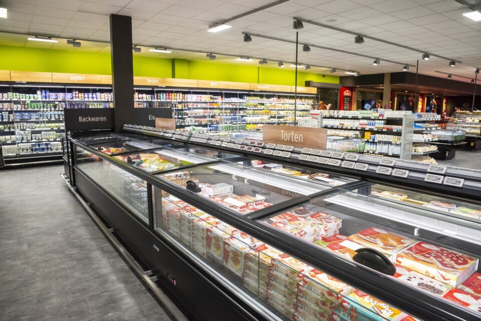 Ein hell erleuchteter WASGAU-Supermarkt mit Kühlvitrinen voller Kuchen und Desserts, beschriftet mit 