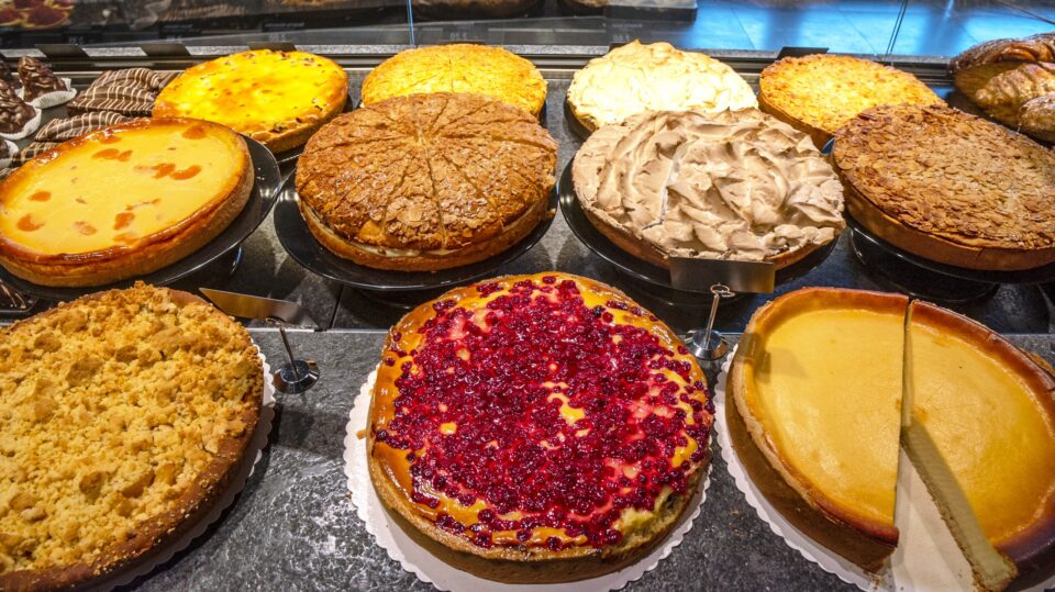 In der WASGAU Bäckerei wird ein Sortiment von ganzen Torten und Käsekuchen mit verschiedenen Belägen wie Beeren, Streusel und Baiser hinter Glas präsentiert.