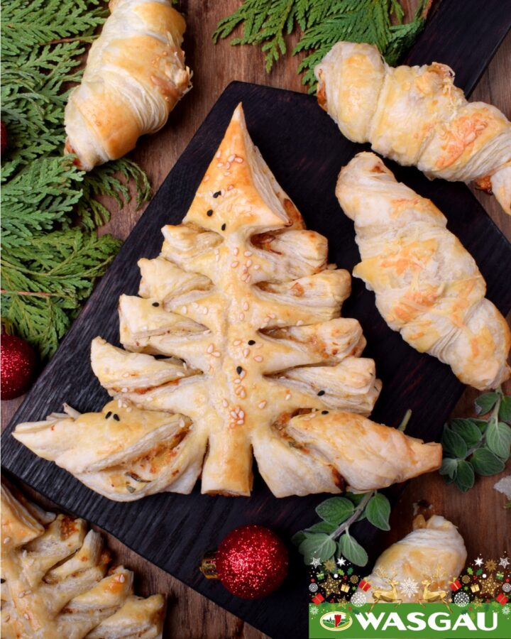 Weihnachtsbaum aus Blätterteig auf einem Holzbrett, umgeben von Croissants und festlicher Dekoration.