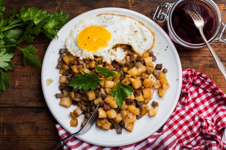 Ein Teller Pyttipanna mit gewürfelten Kartoffeln und Fleisch, garniert mit einem Spiegelei und Petersilie, serviert zusammen mit geschnittenen Rüben.