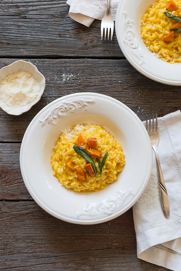 Cremiges Kürbis-Risotto mit geröstetem Kürbis und Salbei, serviert in einer weißen Schale auf einem rustikalen Holztisch.