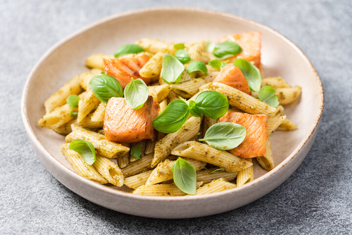 Eine Schüssel Penne-Nudeln mit Pesto, Lachsstückchen, frischen Basilikumblättern und Castellane für eine geschmackliche Abwechslung.