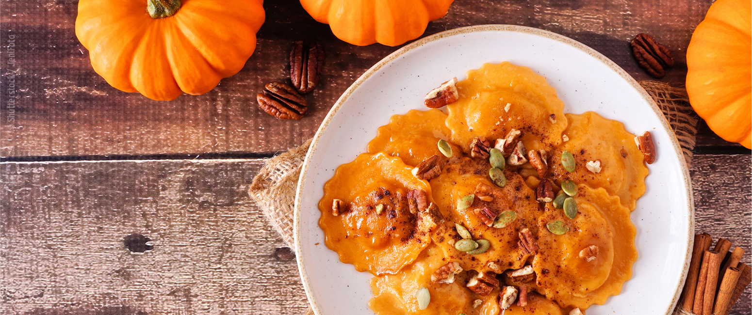Ein Teller mit Kürbisravioli mit Pekannüssen und Kernen, umgeben von Kürbissen auf einem rustikalen Holztisch - perfekt für gemütliche Abende in der KW 44. Entdecken Sie diesen herbstlichen Genuss in unserem aktuellen Prospekt.