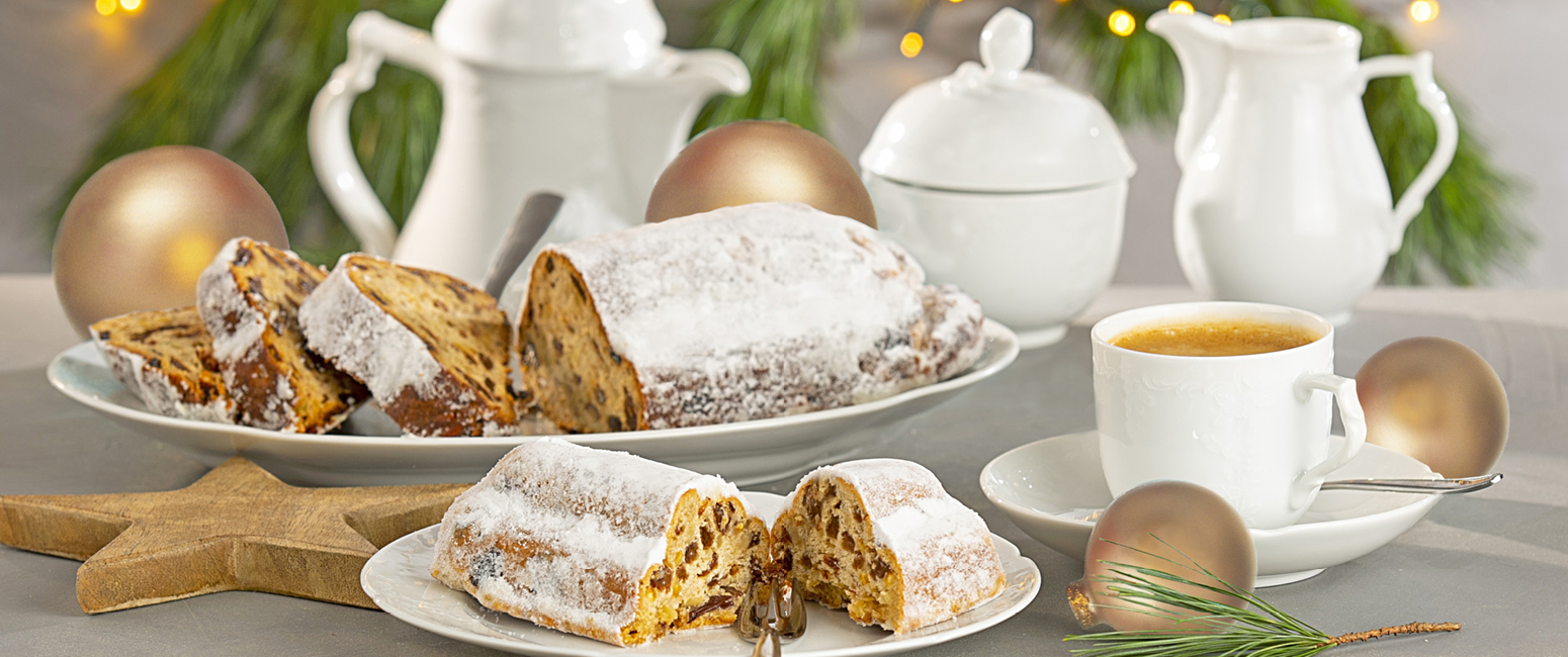 Aufgeschnittener Stollen, eine Tasse Tee und weihnachtliche Dekoration auf einem festlich gedeckten Tisch mit weißem Porzellan schaffen eine bezaubernde Weihnachtsszene in der Prospekt KW 45.