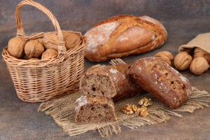 Ein Korb mit Walnüssen und geschnittenem Vollkornbrot auf Sackleinen, mit Walnussbrötchen, zusätzlichen Walnüssen und einem Laib im Hintergrund.