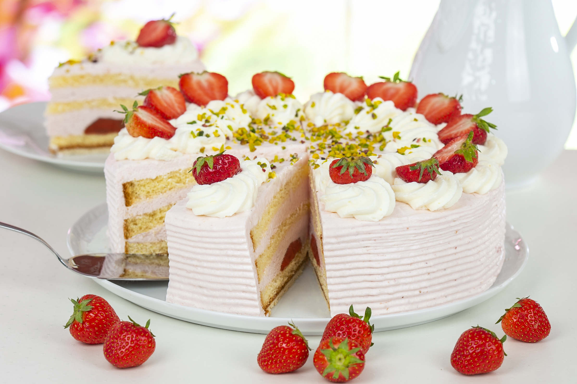 Ein geschichteter Erdbeerkuchen mit Sahne und Erdbeeren, garniert mit Pistazien, auf einem weißen Teller.